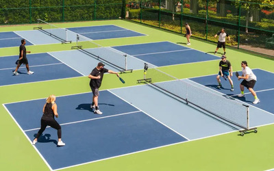 Aerial view of 3 outdoor pickleball courts with the 2 closest courts being used in active play by middle-aged players.