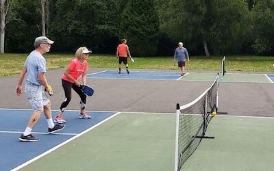An older white couple waiting for a pickleball serve in an outdoor court.